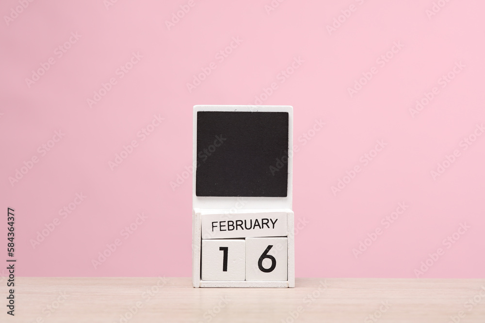 White wooden block monthly calendar with the date february 16 on the table, pink background. Planning, business concept