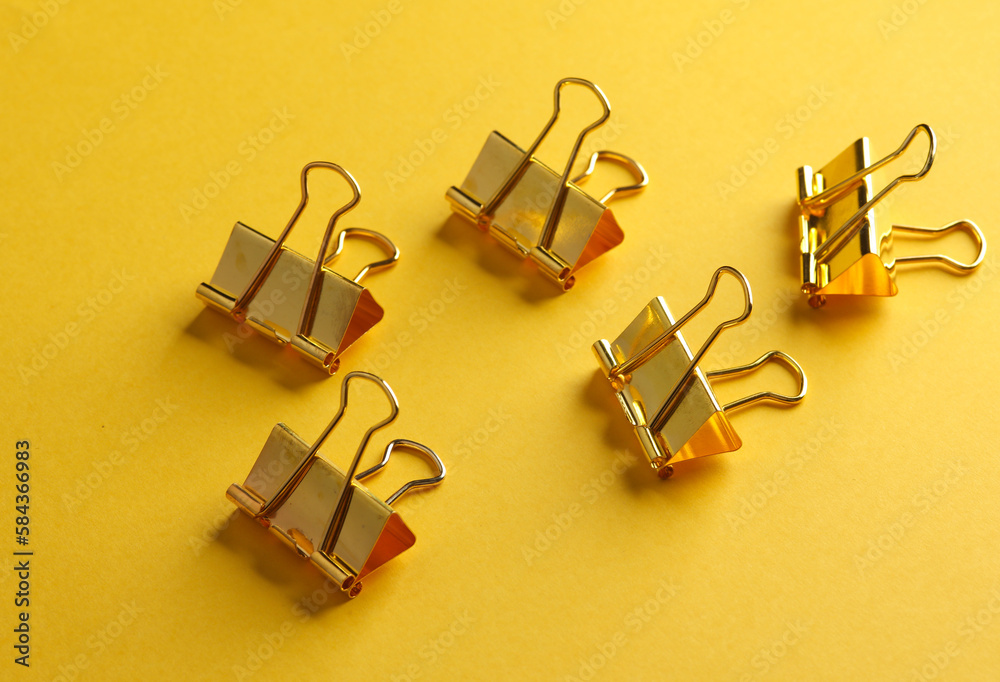 Golden paper binder clips on yellow background Golden paper binder clips on yellow background