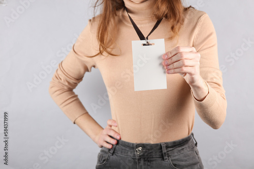 Young woman wearing Identification white blank id card on gray background