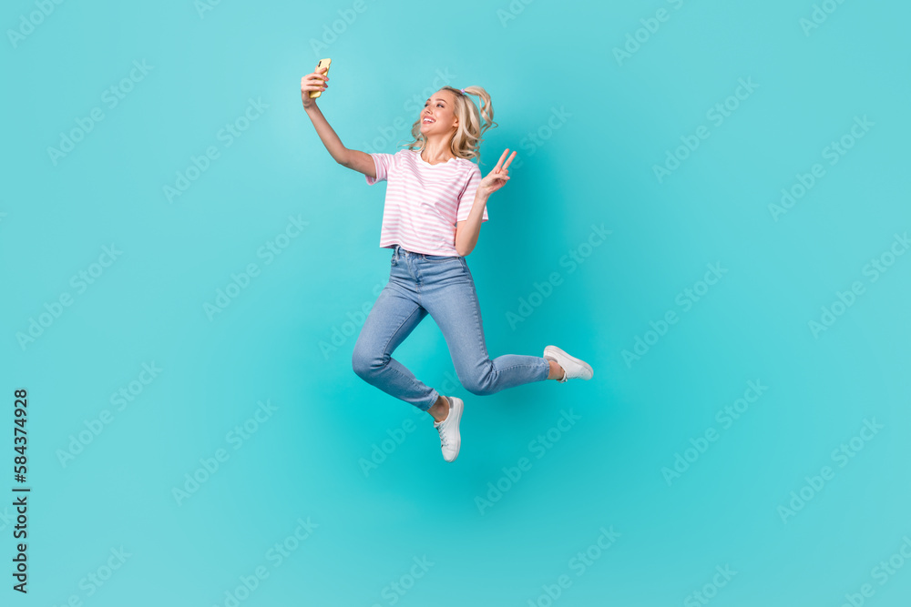 Full size photo of charming girl blond hair casual t-shirt doing selfie on phone show v-sign isolated on bright teal color background