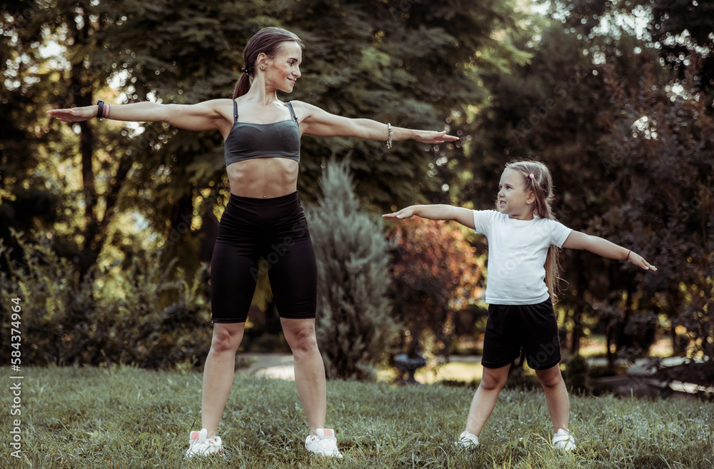 Active family concept. Fit mom with little daughter practice outdoor exercises in the park. Healthy lifestyle. Physical Education Active family concept. Fit mom with little daughter practice outdoor exercises in the park. Healthy lifestyle. Physical Education