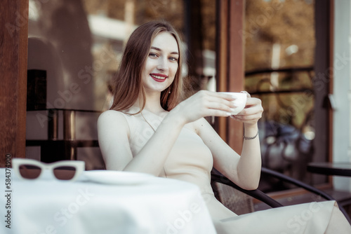 Young smiling woman with coffee cup sitting at a table in outdoor cafe