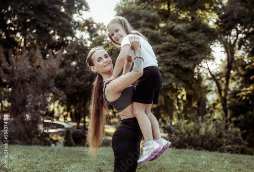 Maternal love and care. Fit mom holds her little daughter in her arms in the park. Healthy lifestyle, fitness