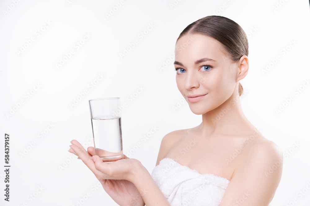 Natural young woman in white towel holds glass of water, concept water balance and women's health, cosmetic procedures to preserve youth, in the studio on a light background Natural young woman in white towel holds glass of water, concept water balance and women's health, cosmetic procedures to preserve youth, in the studio on a light background