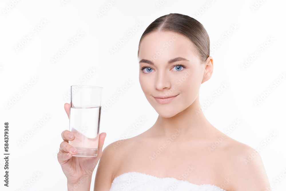 Natural young woman in white towel holds glass of water, concept water balance and women's health, cosmetic procedures to preserve youth, in the studio on a light background Natural young woman in white towel holds glass of water, concept water balance and women's health, cosmetic procedures to preserve youth, in the studio on a light background