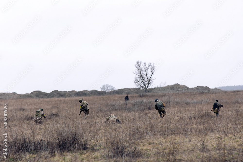 Group of armed Ukrainian soldiers runs through steppe.
