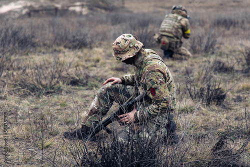 Two armed Ukrainian soldiers sit and rest in steppe against background of dry grass.