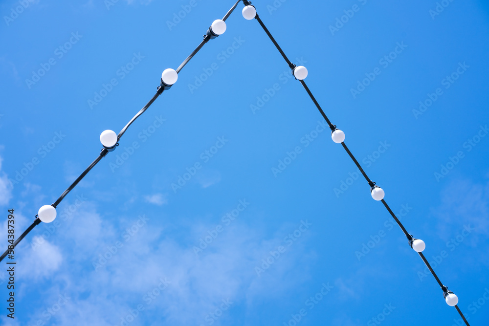 White energy-saving light bulbs on a wire, blue sky, a beautiful decoration for the evening city White energy-saving light bulbs on a wire, blue sky, a beautiful decoration for the evening city