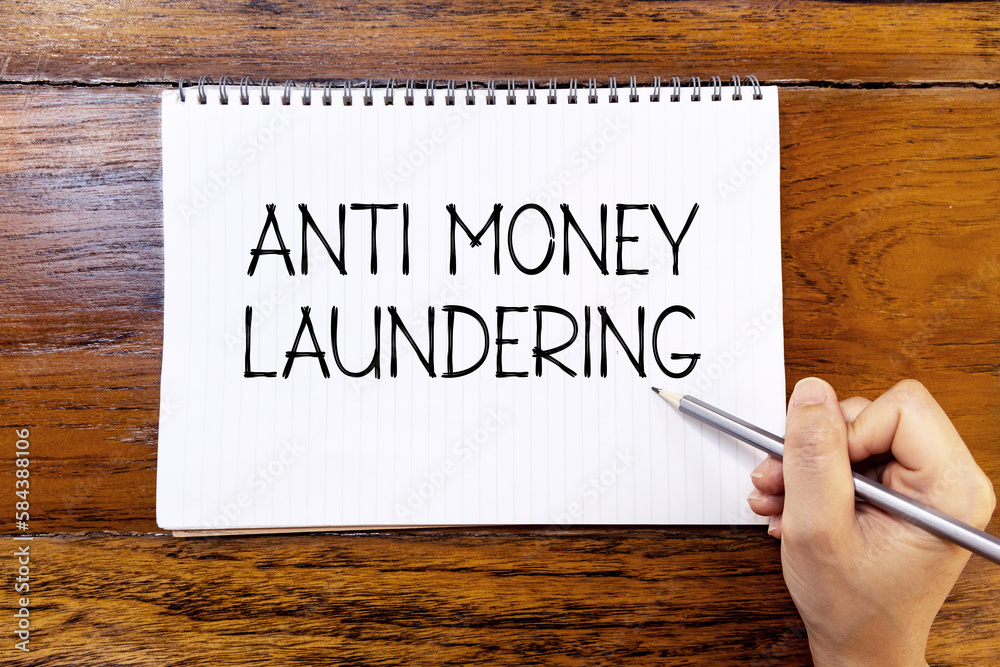 Anti money laundering handwriting text on blank notebook paper on wooden table with hand holding pencil. Business concept about anti money laundering. Anti money laundering handwriting text on blank notebook paper on wooden table with hand holding pencil. Business concept about anti money laundering.