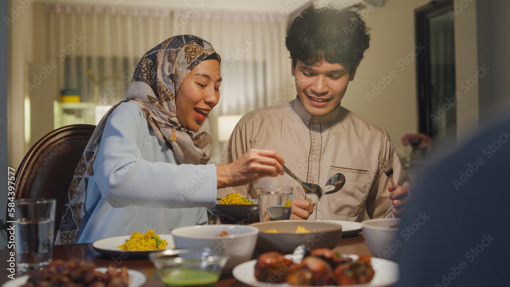 Happy Asia muslim sweet housewife serve halal food biryani rice to husband in Ramadan dinner together at dining table. Family celebration end of Eid al-Fitr togetherness, Hari Raya family reunion.