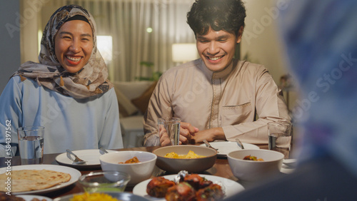 Close-up Happy Asia muslim wife talk to husband Ramadan dinner together at home. Family of two generation catering celebration end of Eid al-Fitr togetherness at home. Hari Raya family reunion.