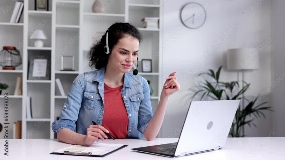 Young curly brunette woman wearing video call headset on laptop in home light office. Video conference, remote meeting. Programmer, remote work, work from home. Young curly brunette woman wearing video call headset on laptop in home light office. Video conference, remote meeting. Programmer, remote work, work from home.
