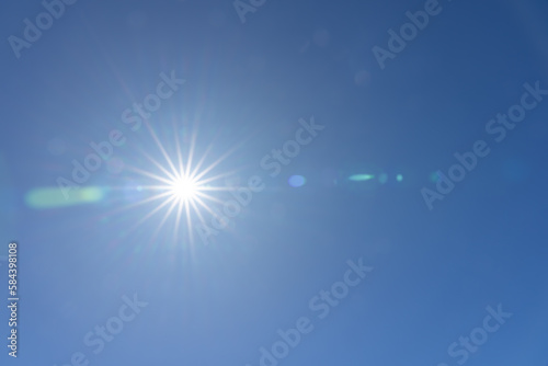 Sun flare in clear blue sky above with lens flare effect 