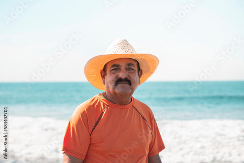 close up senior adult with hat and mustache looking at the camera on the beach at noon