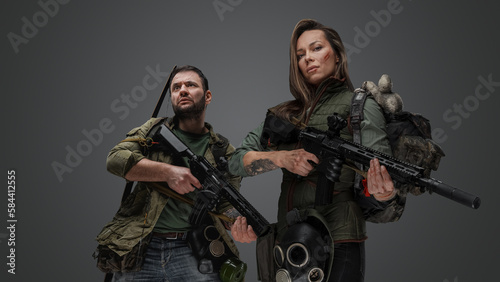 Studio shot of post apocalyptic couple survivors with guns against gray background.