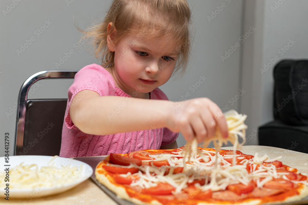 Small child cooking at home sitting at the table. Little girl making pizza in the kitchen. Small child cooking at home sitting at the table. Little girl making pizza in the kitchen.