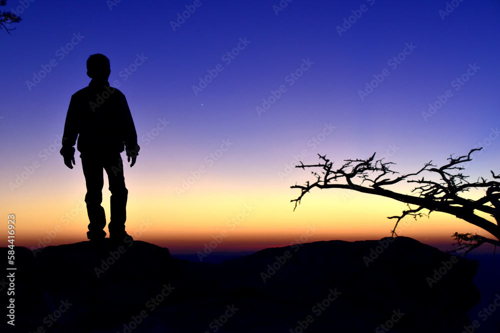 silhouette of a person standing on a rock with brilliant sunset