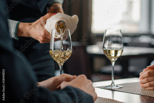 A date in a hotel restaurant a man and a woman drink white wine in glasses the waiter pours wine from a bottle