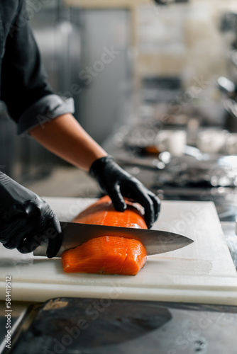 Professional kitchen in the hotel restaurant The chef cuts a large fresh salmon carcass with a knife © Guys Who Shoot