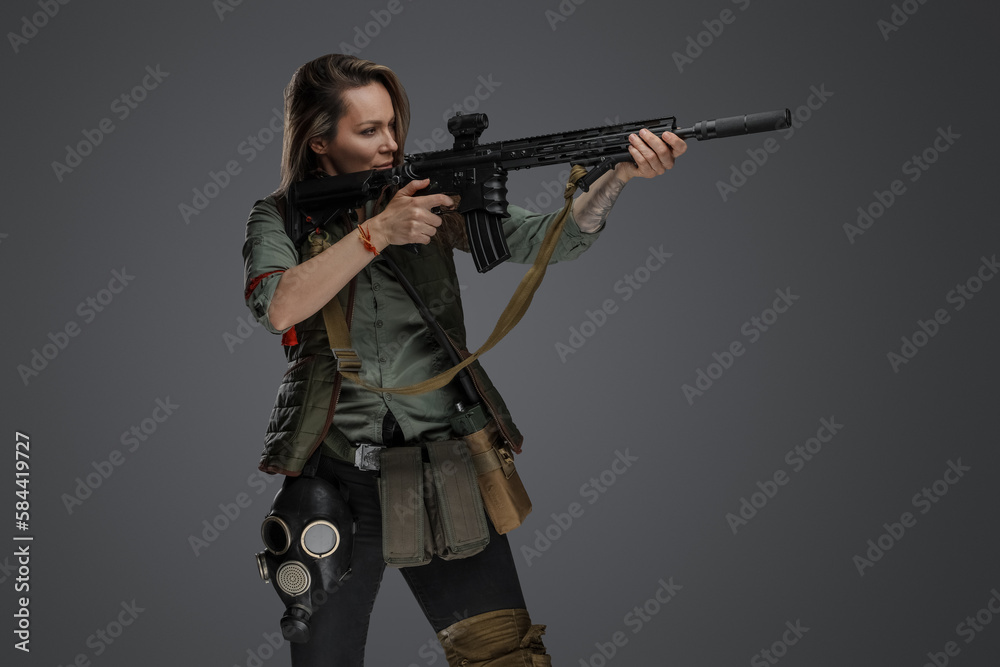 Portrait of military woman with rifle looking to side isolated on grey background.