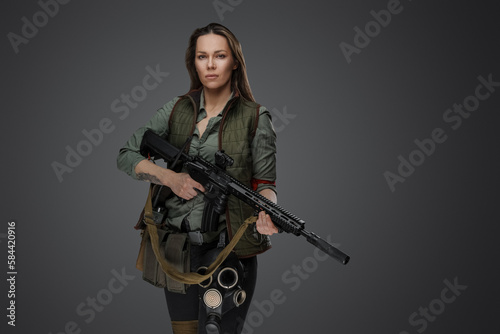 Studio shot of professional killer woman with rifle in setting of post apocalypse.