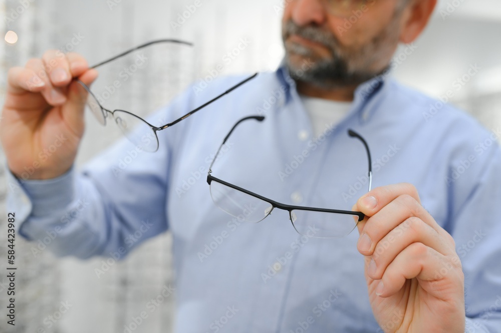 Senior man choosing glasses in optical store, try on eyeglass frames to decide on the perfect one Senior man choosing glasses in optical store, try on eyeglass frames to decide on the perfect one
