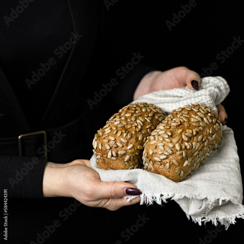 Two loaves of multigrain bread on towel in hands of oman. Bread with sunflower seeds. Fresh bakery. Healthy diet. Black background. Side view. Copy space. © Artur