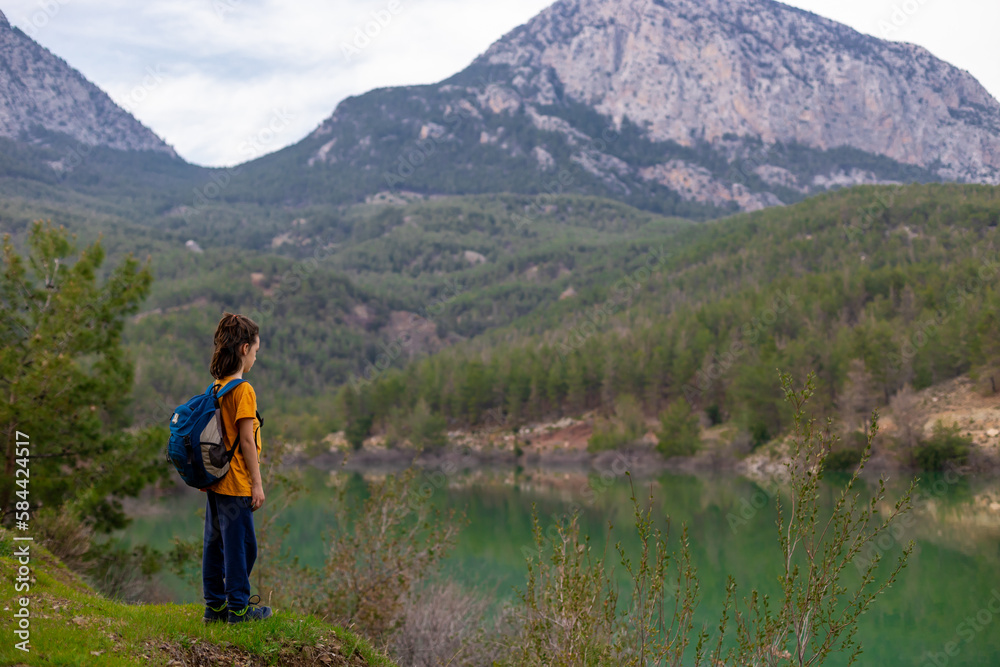 A child with a backpack looks at a beautiful mountain lake. Relaxed, peaceful, thoughtful, happy and free on a mountain lake.