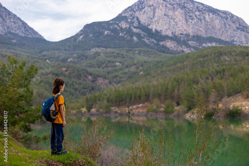 A child with a backpack looks at a beautiful mountain lake. Relaxed, peaceful, thoughtful, happy and free on a mountain lake. © zhukovvvlad
