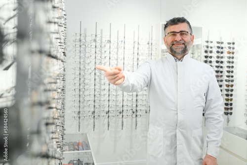 Portrait of a handsome ophthalmologist in front of the showcase with eyeglasses in the hospital.