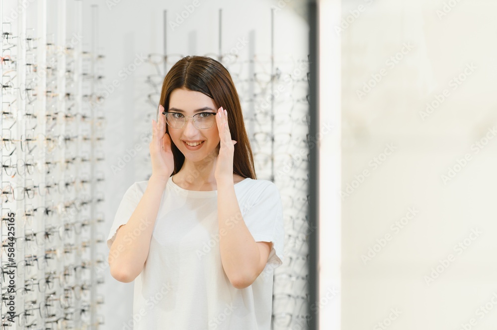 eyesight and vision concept - young woman choosing glasses at optics store. eyesight and vision concept - young woman choosing glasses at optics store.