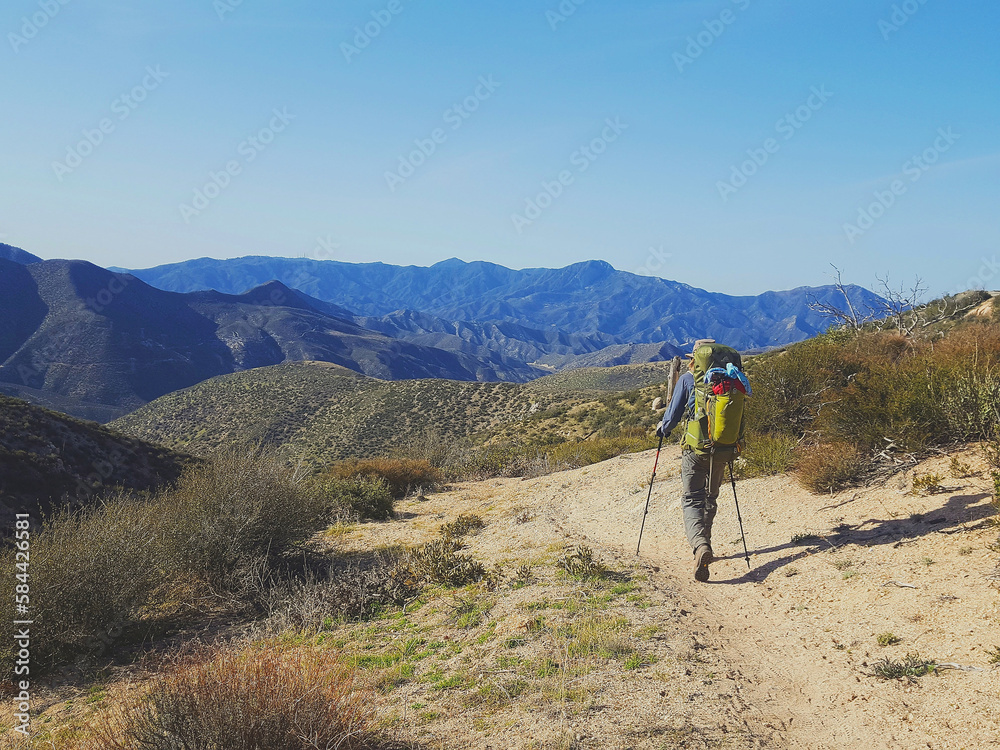 Male backpacker hiking through the California desert with mountains and desert plants