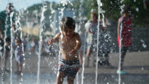 One happy small boy running toward water jets at outdoor park during summer vacations