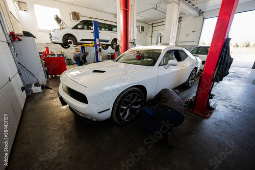 Mechanic in service repair station working with muscle car. Man worker diagnose the chassis.