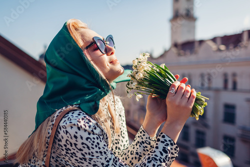 Stylish young woman wearing green retro shawl with sunglasses smelling spring flowers. Classic vintage outdoor fashion