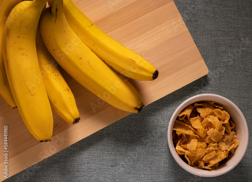 Bananas on wooden cutting board with cereal on white cup