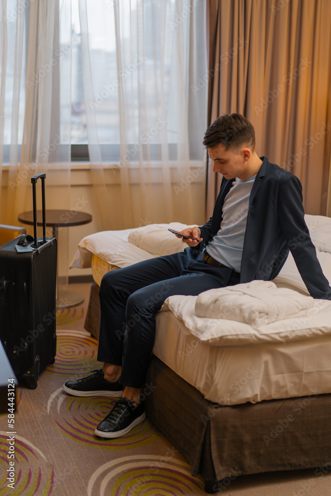 Man with suitcase sitting on bed in hotel room while traveling recreation concept