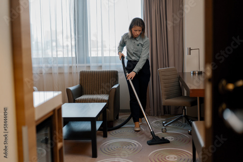 Картината върху платно A diligent maid in uniform carefully vacuums the carpet while cleaning a hotel r