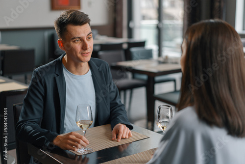 A date in a hotel restaurant, a man and a woman drink white wine in glasses the face of a serious man