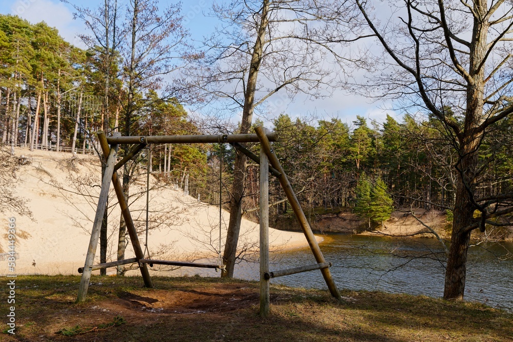 Large wooden swing against the backdrop of the lake. Sunny day in the forest.