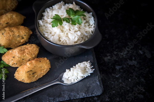 Bolinhos de bacalhau, very famous in Portuguese gastronomy. Fried dumpling, cod dumpling, fish, salted cod fritters, bacalao bunuelos. Codfish cake served with white rice on a dark background. photo