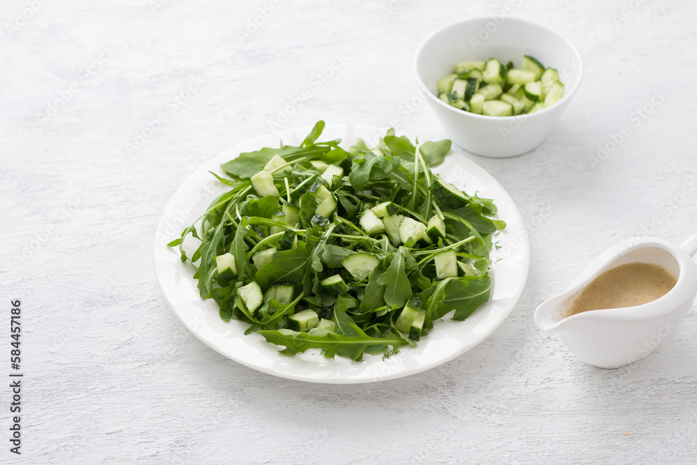 A plate with arugula , chopped dill, cucumber and a yoghurt dressing on a light gray background. Cooking delicious homemade salad A plate with arugula , chopped dill, cucumber and a yoghurt dressing on a light gray background. Cooking delicious homemade salad