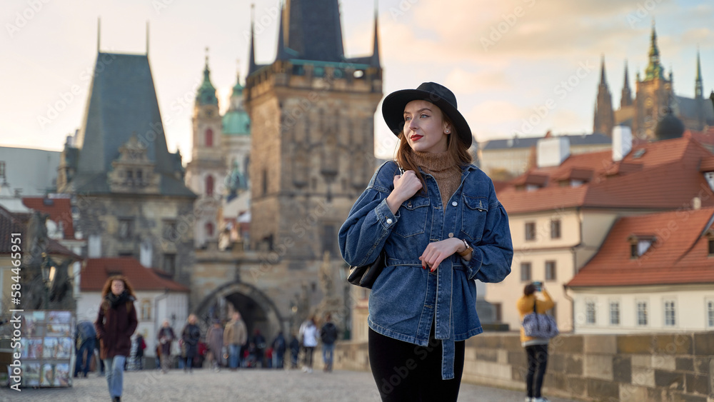Female traveller tourist on the Charles Bridge in Prague, Czezh Repubic. Stylish beautiful young woman earing black hat. Elegant retro lady fine art portrait.