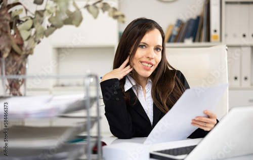 Portrait of cheerful woman office worker sitting at table and doing her daily paperwork.