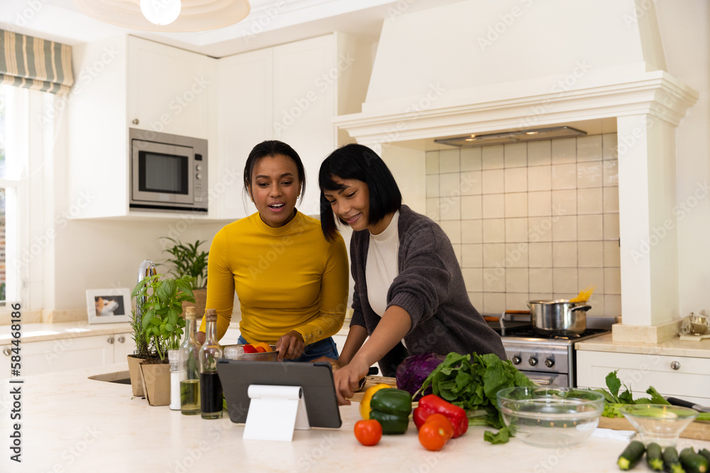 Happy biracial sisters cooking in kitchen and using tablet Happy biracial sisters cooking in kitchen and using tablet