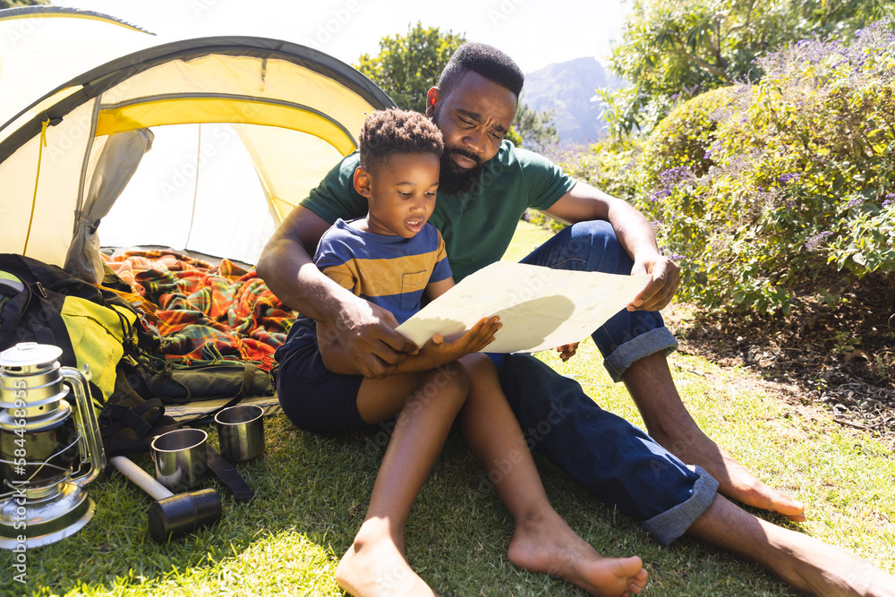 happy-african-american-father-and-son-sitting-on-grass-and-reading-map