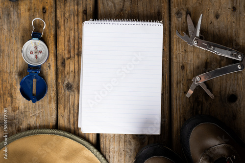 Camping equipment of compass, pocket knife and blank notebook on wooden background with copy space