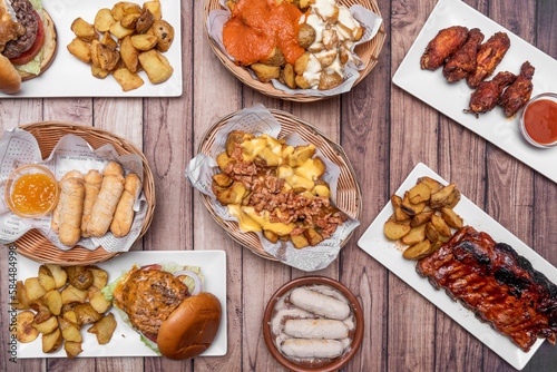 Set of international fast food dishes, barbecue ribs, hamburgers, patatas bravas, Venezuelan teques, chicken wings with sauce and french fries with bacon and cheese photo