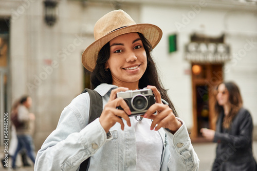 Adventurous young Latina captures the vibrant beauty of a new city on her stylish hat and camera.