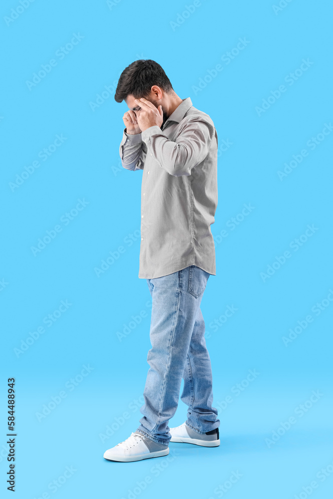 Young man suffering from loud noise on blue background Young man suffering from loud noise on blue background